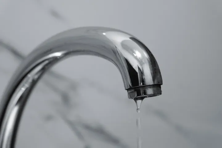 З носика хромованого змішувача капає вода